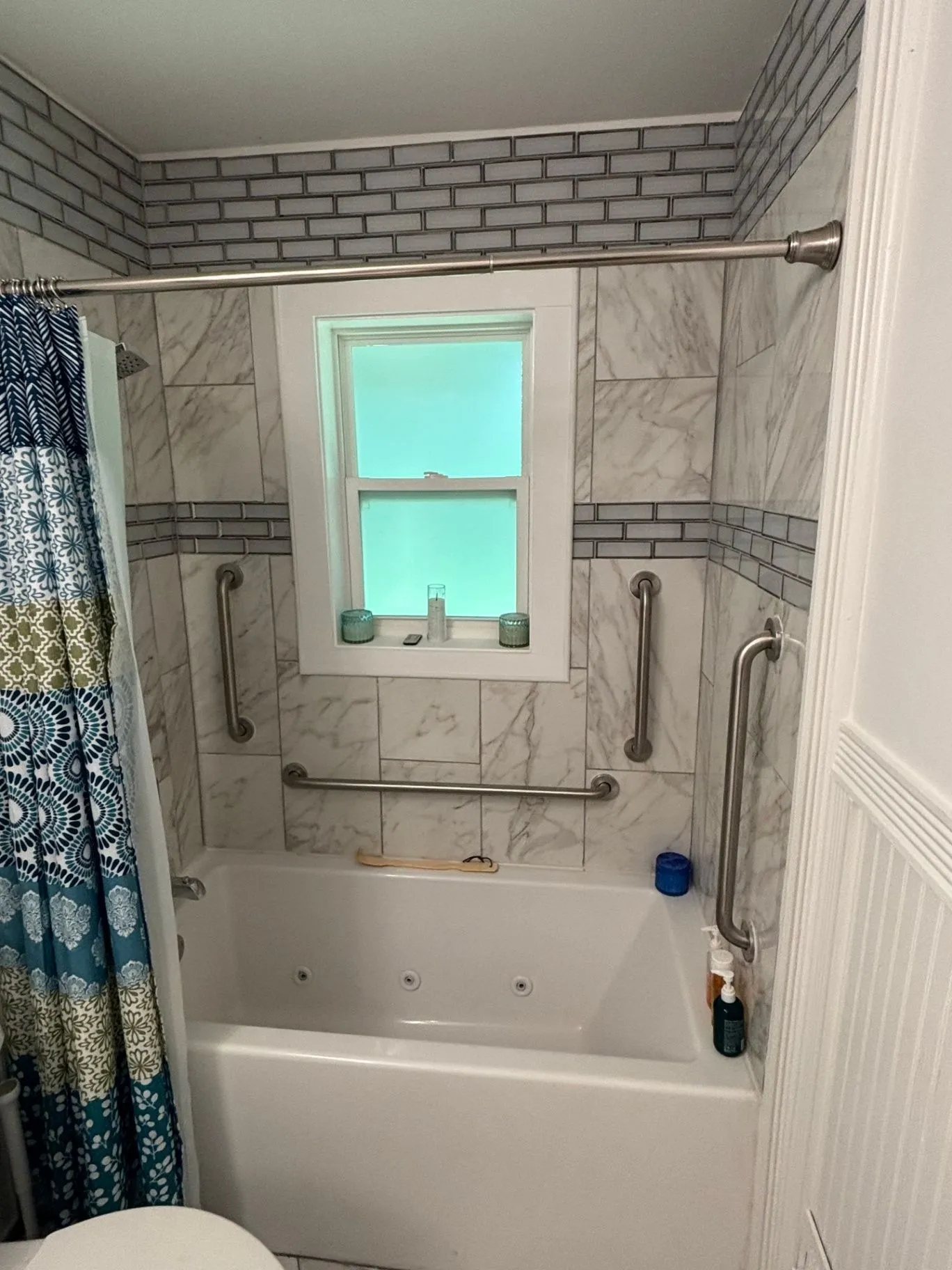Full-height view of a tiled bathtub and shower area showing vertical and horizontal grab bars, the tub, and a shower curtain