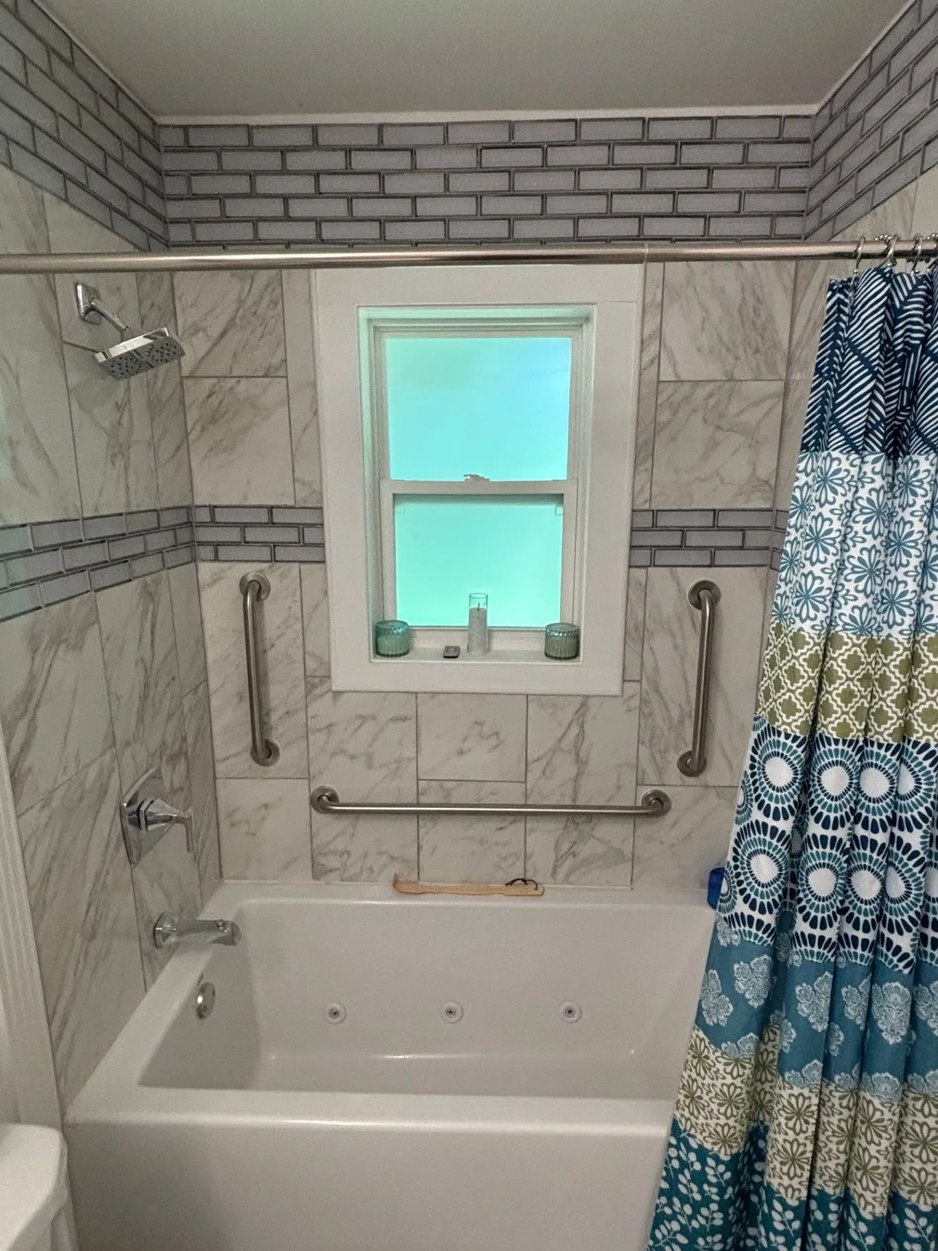 Alternate view inside a tiled bathtub and shower showing the showerhead, faucet, vertical grab bars, and horizontal grab bar