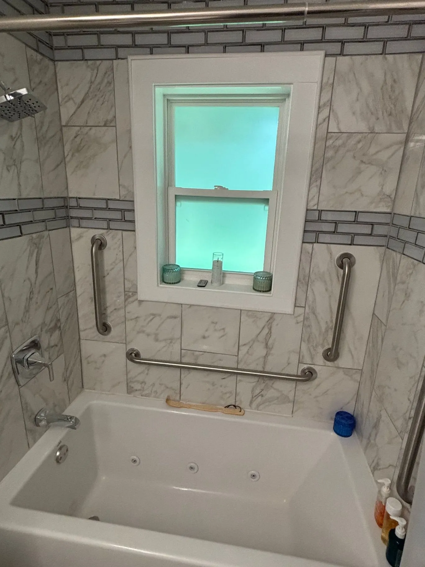 Detail view of the showerhead, faucet, and grab bars installed on a tiled bathtub and shower surround