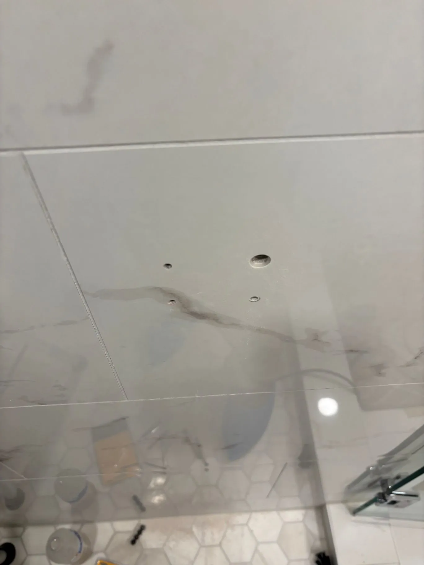 Tiled shower wall with drilled mounting holes and installation tools visible below