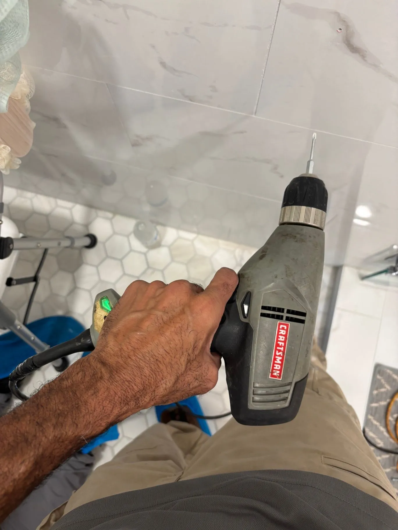 Hand using a drill against the tiled shower wall during installation
