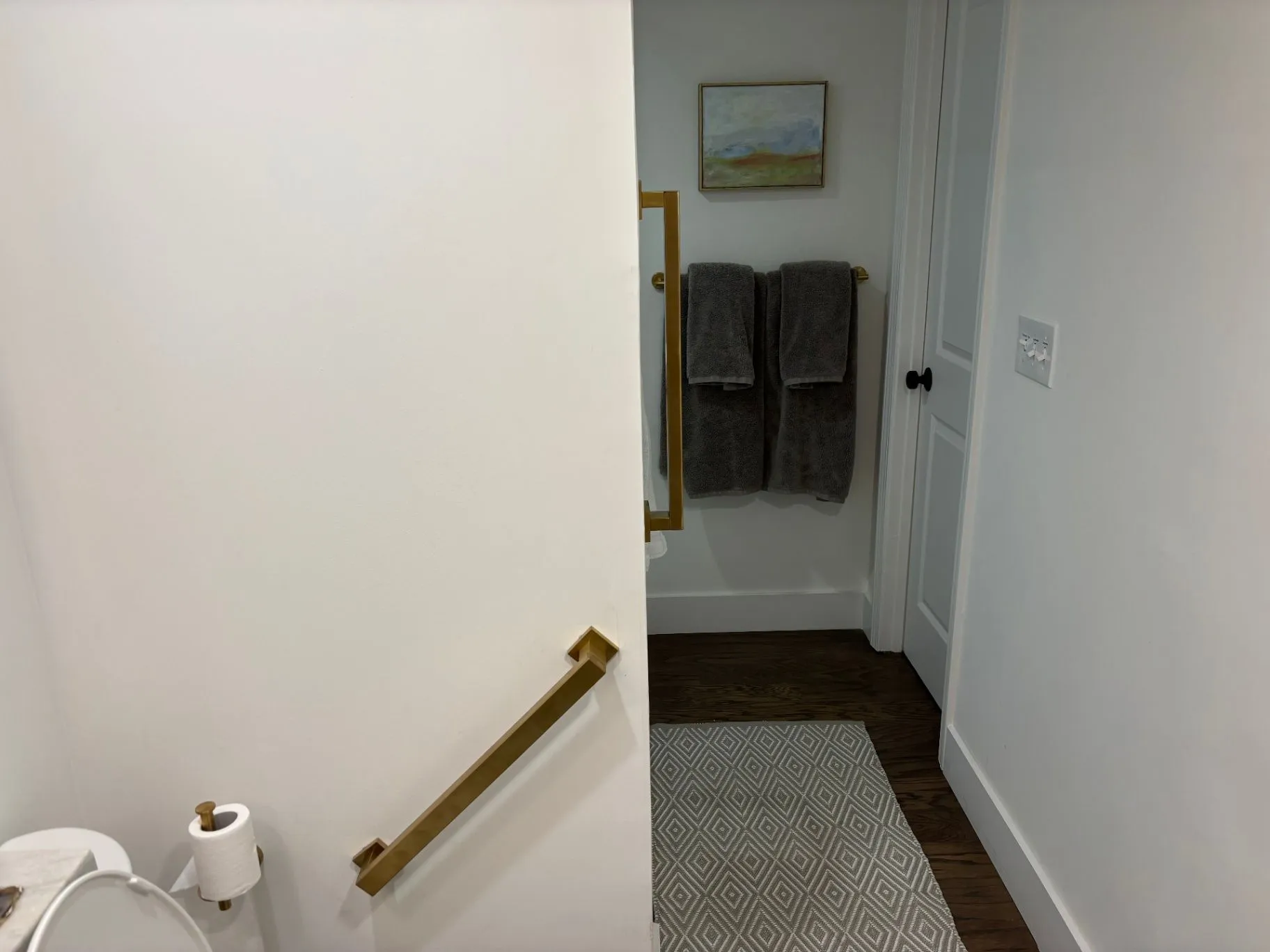 Bathroom view showing gold grab bars beside a toilet and near the shower entrance
