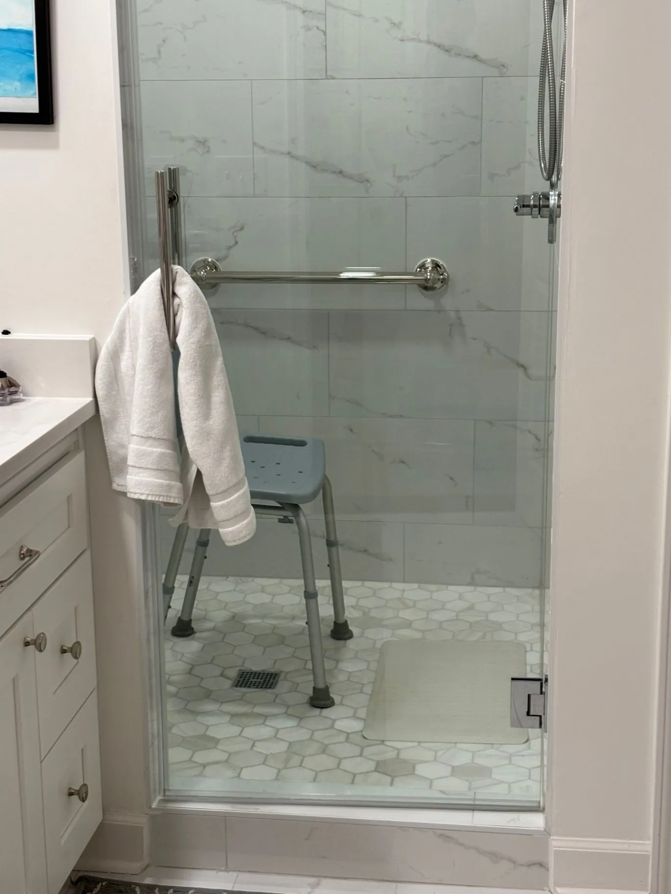 Completed tiled shower with a horizontal grab bar, shower chair, handheld shower, and floor drain