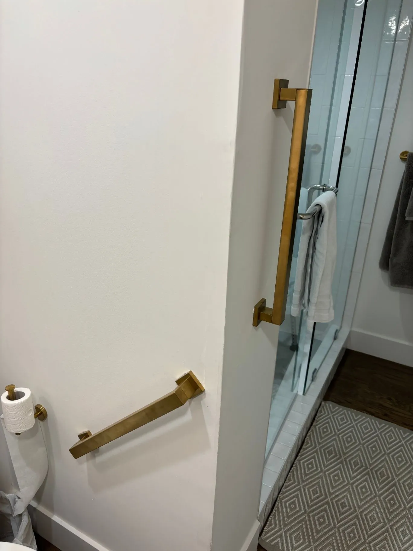 Gold grab bars installed beside a toilet and at the shower entrance