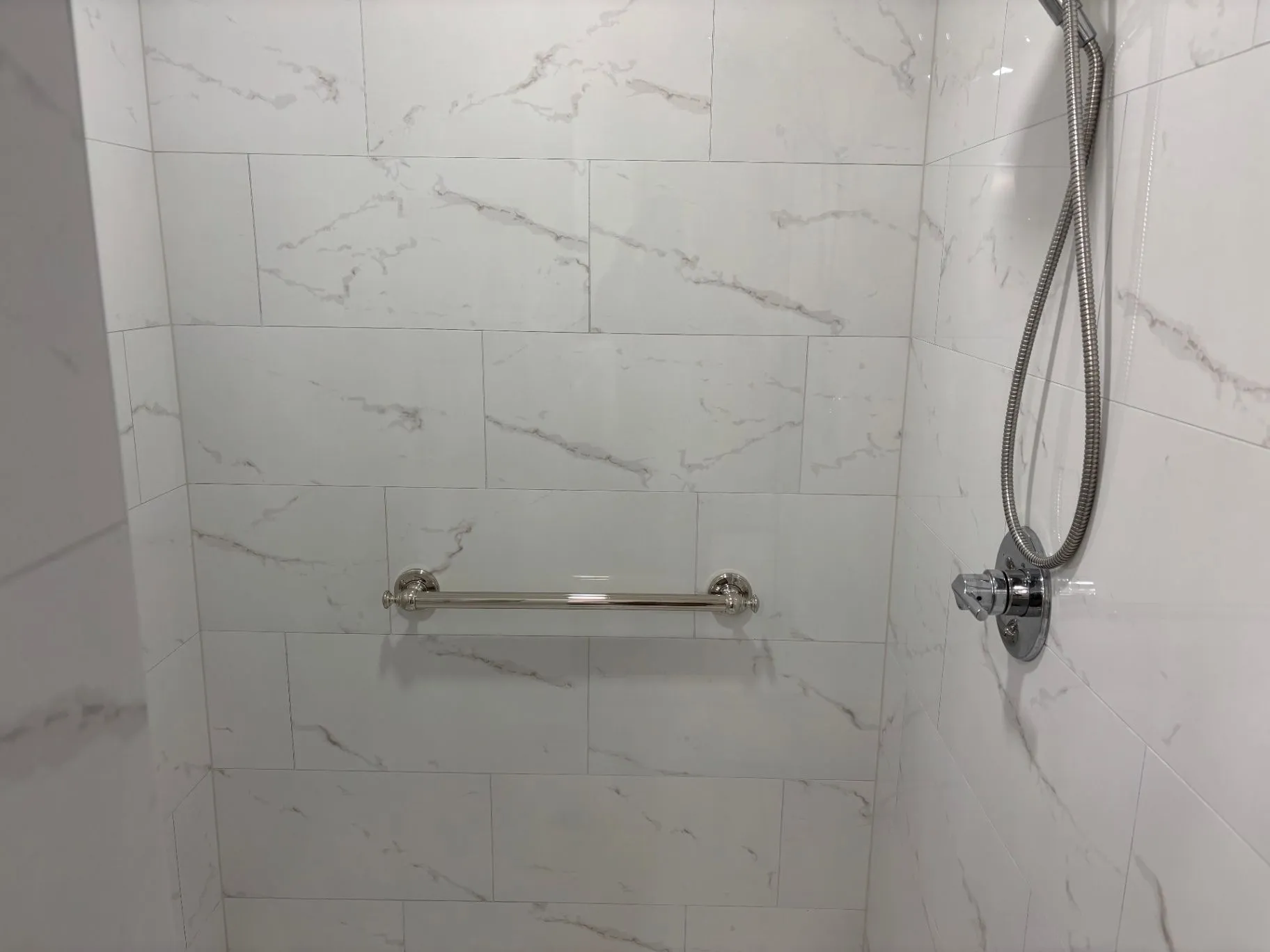 Close view of a horizontal grab bar and handheld shower control on a tiled shower wall