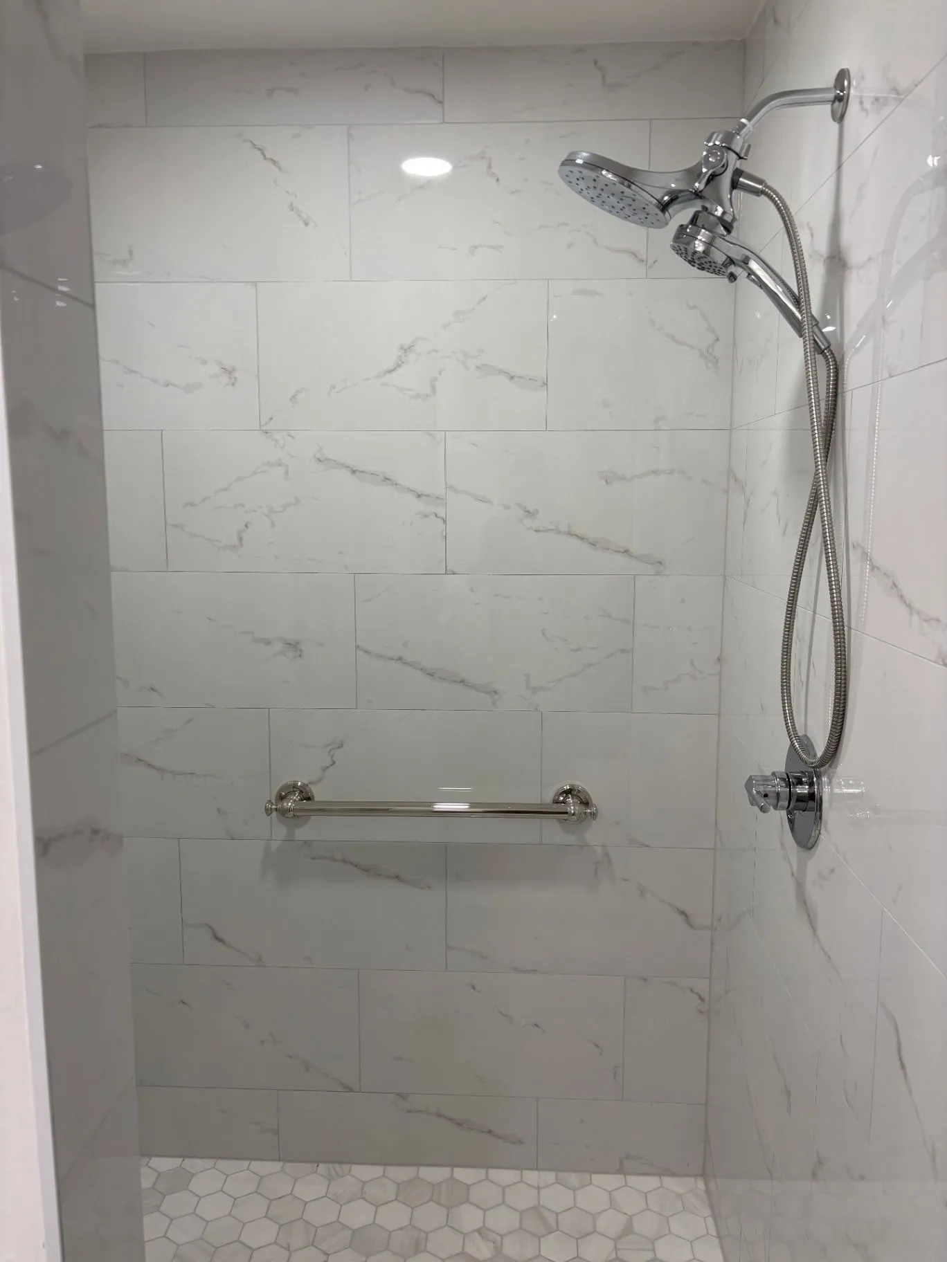 Completed tiled shower with a horizontal grab bar and handheld shower