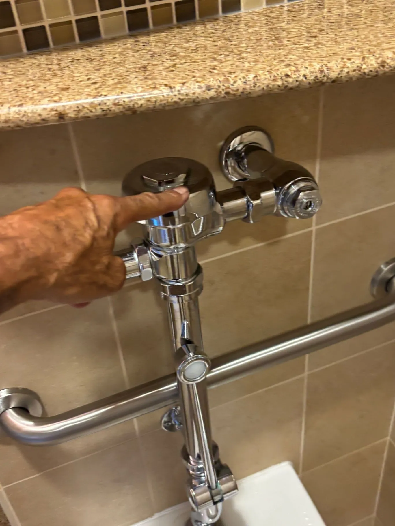 Close view of a chrome bathroom plumbing fixture and horizontal grab bar against tiled walls